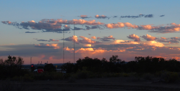 [Clouds ranging in color from white to dark blue pepper the sky above the trees on the ground.]